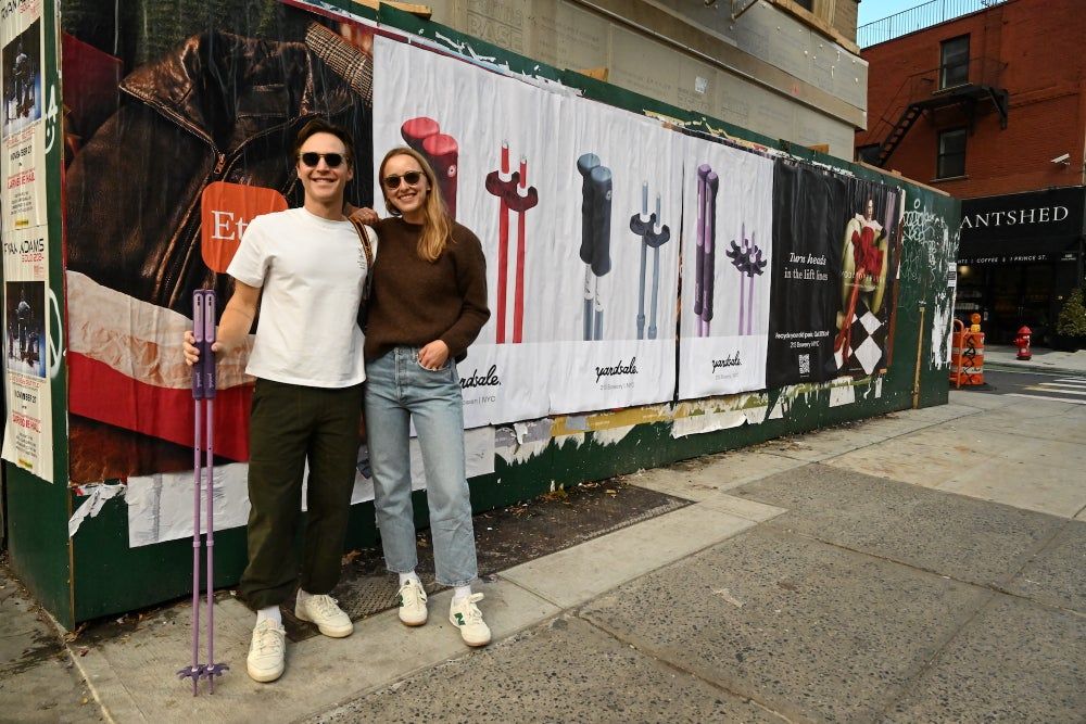 An image of two people smiling in front of a billboard