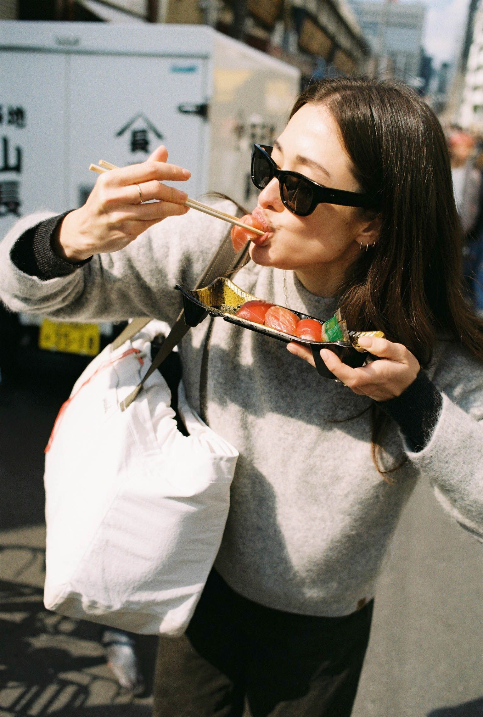 An image of a woman eating sushi with a 20L Day Bag on her shoulder
