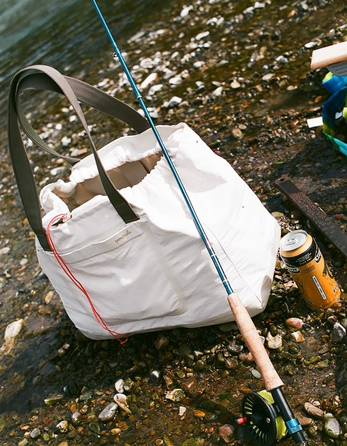 An image of a bag on a river bank with a fishing rod