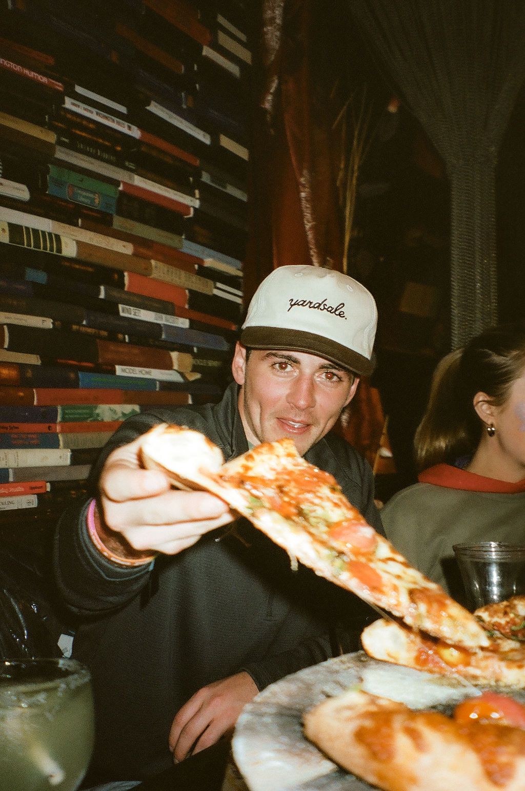 An image of person in a hat offering a slice of pizza